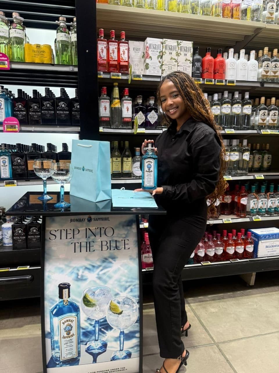 A promoter behind the tasting table with copa glasses and the gift bag out, the Step Into The Blue banner facing the aisle