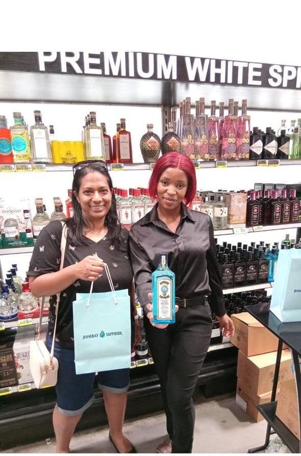 A promoter presenting the bottle to a shopper holding her gift bag, under the store's premium white spirits sign