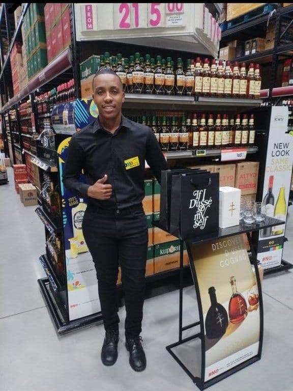 A promoter giving a thumbs up beside the stand, the gift bag and box set out on its shelf
