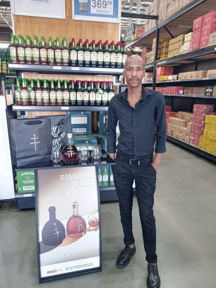 A promoter standing beside the Discover D'Ussé banner and a tasting table holding the decanter, glasses and gift bags