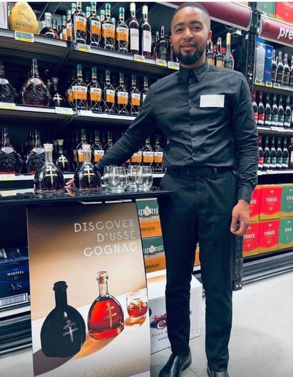 A promoter at the tasting table with the decanter and glasses out, the Discover D'Ussé banner facing the aisle