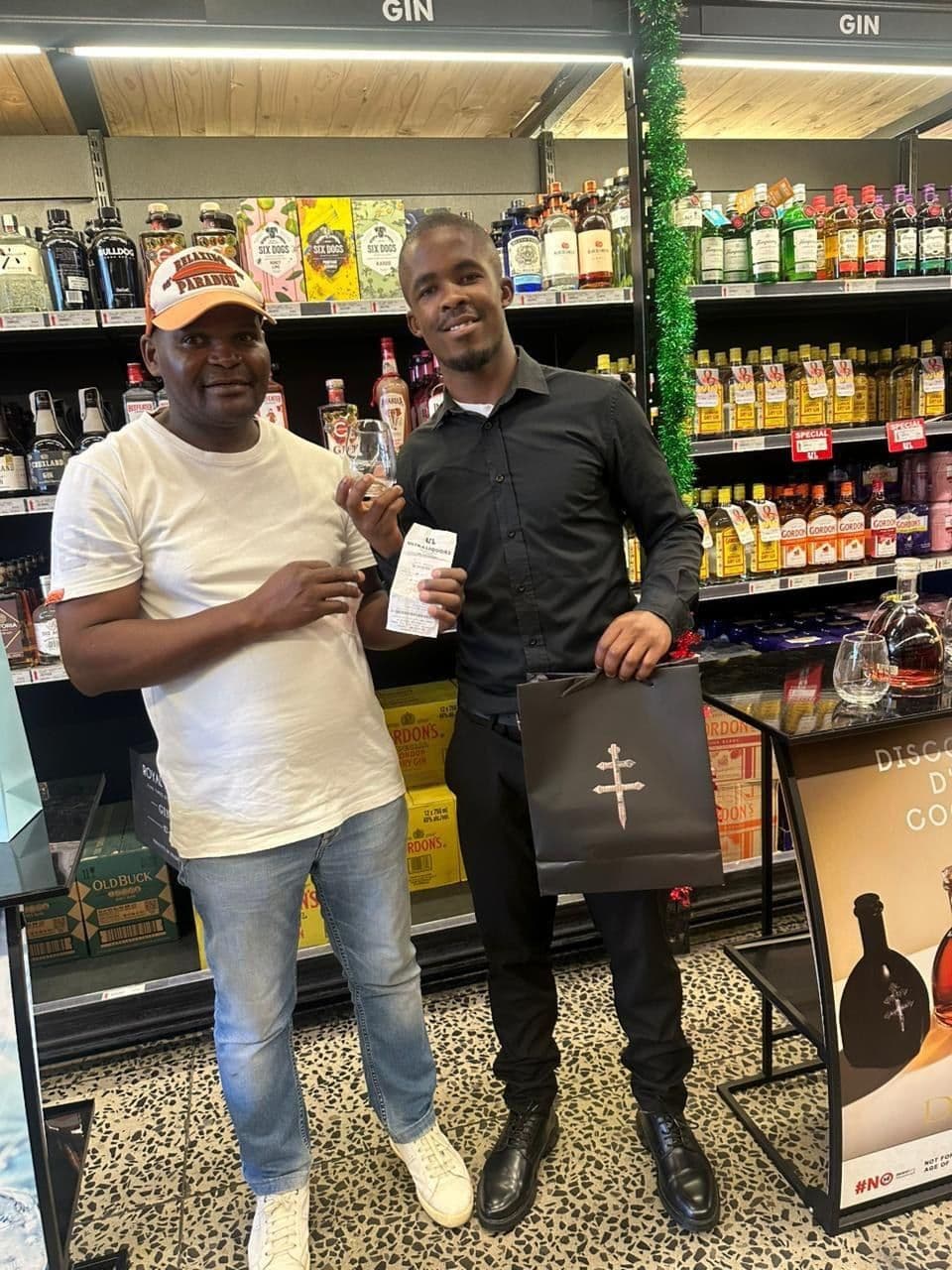 Two shoppers with the black D'Ussé gift bag between them, posing in front of the tasting stand