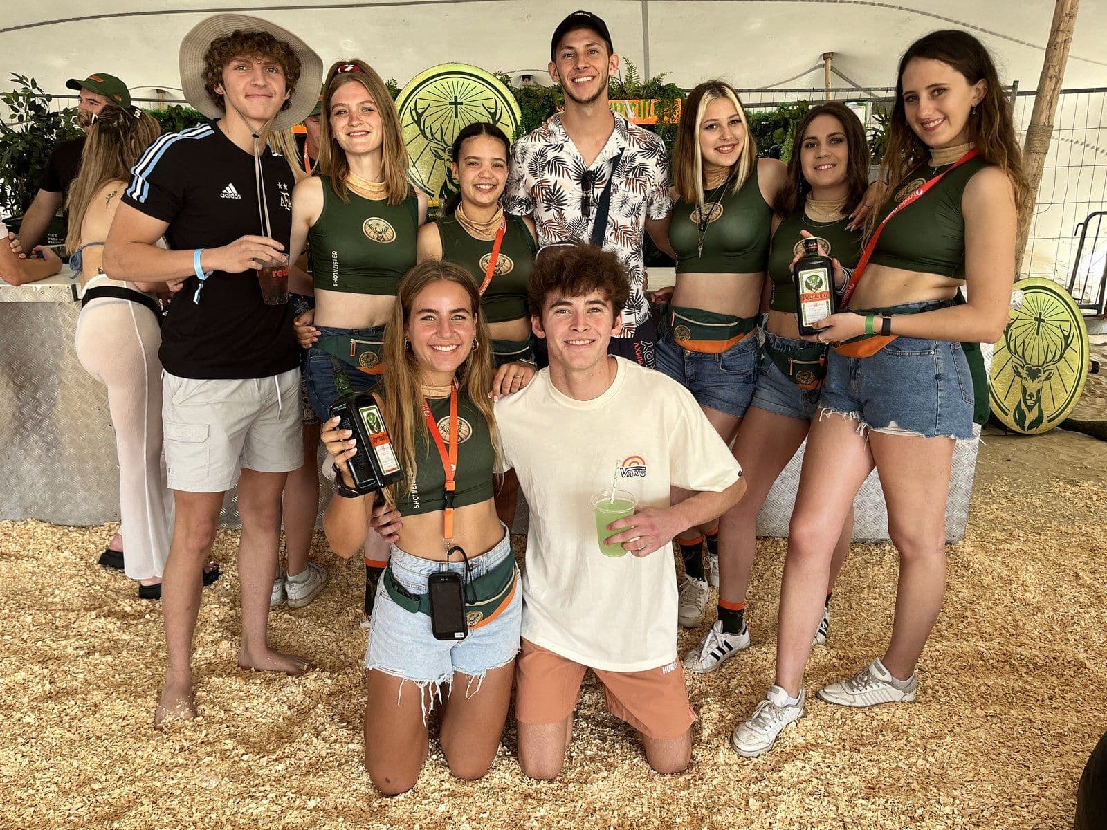 Jägermeister ambassadors and guests posing together in front of the Shotmeister bar under a stretch tent, bottles and cups in hand