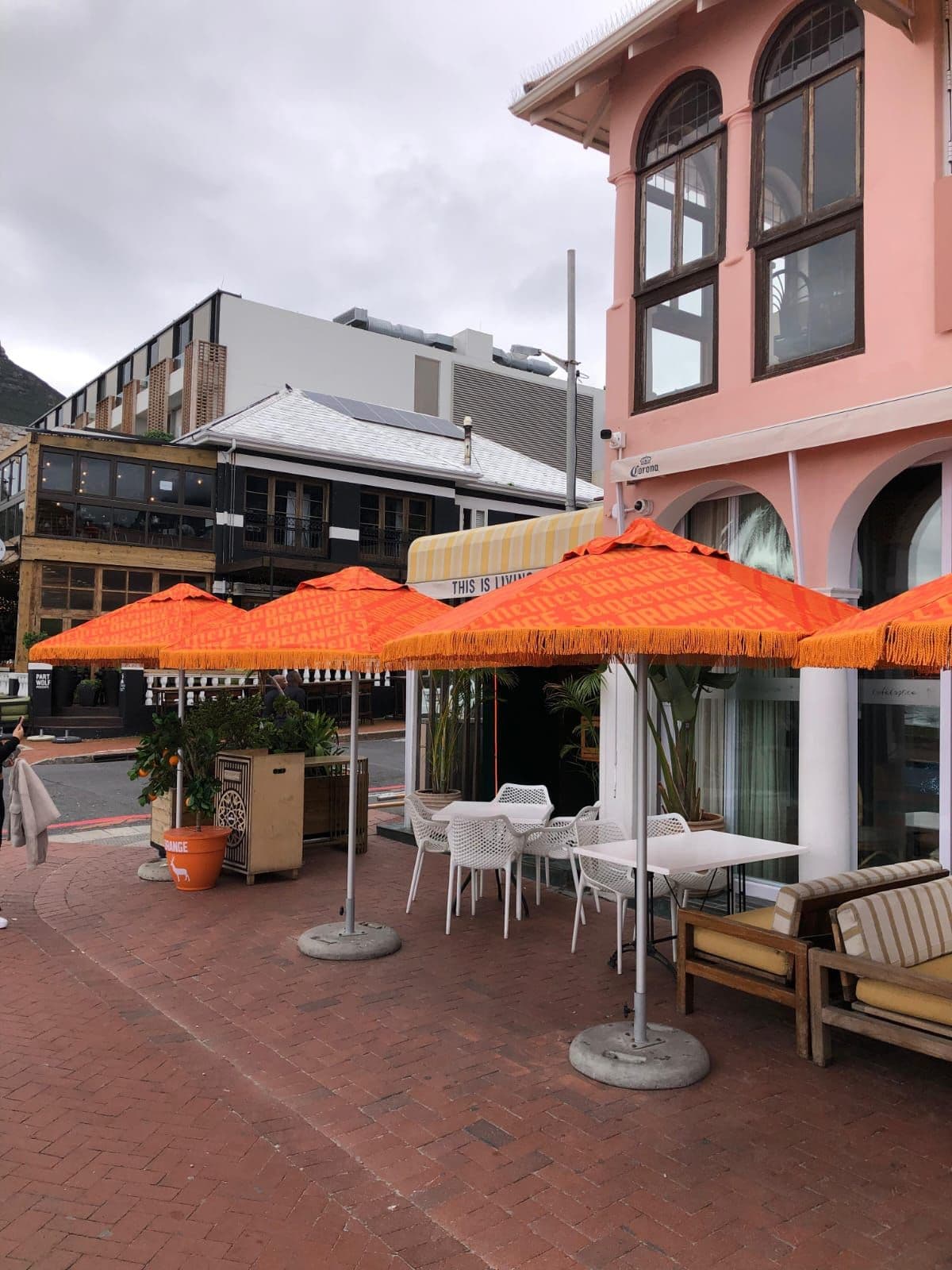 A restaurant terrace branded for Jägermeister Orange: a run of four orange fringed parasols printed with the Jägermeister Orange wordmark over white outdoor tables and chairs, with a branded orange planter carrying the stag mark in the foreground