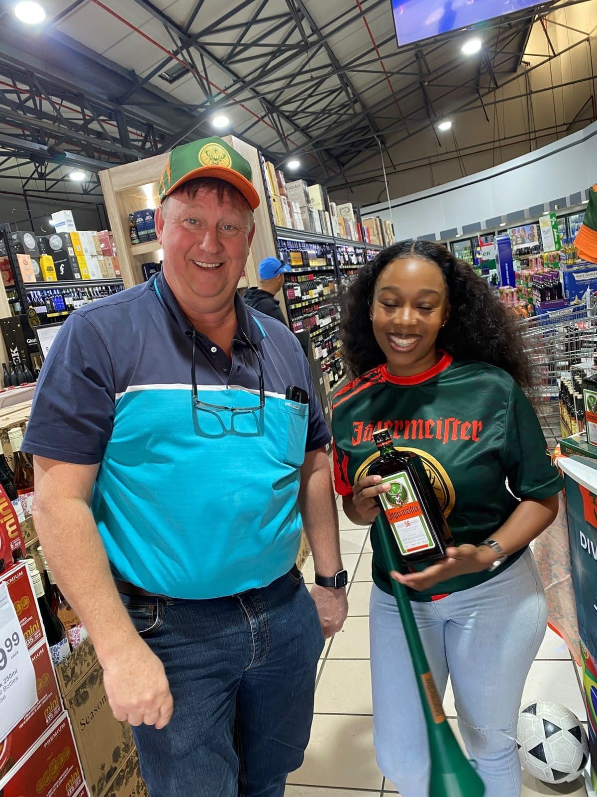 An older shopper in a teal polo with a promoter holding the flag, a football at their feet