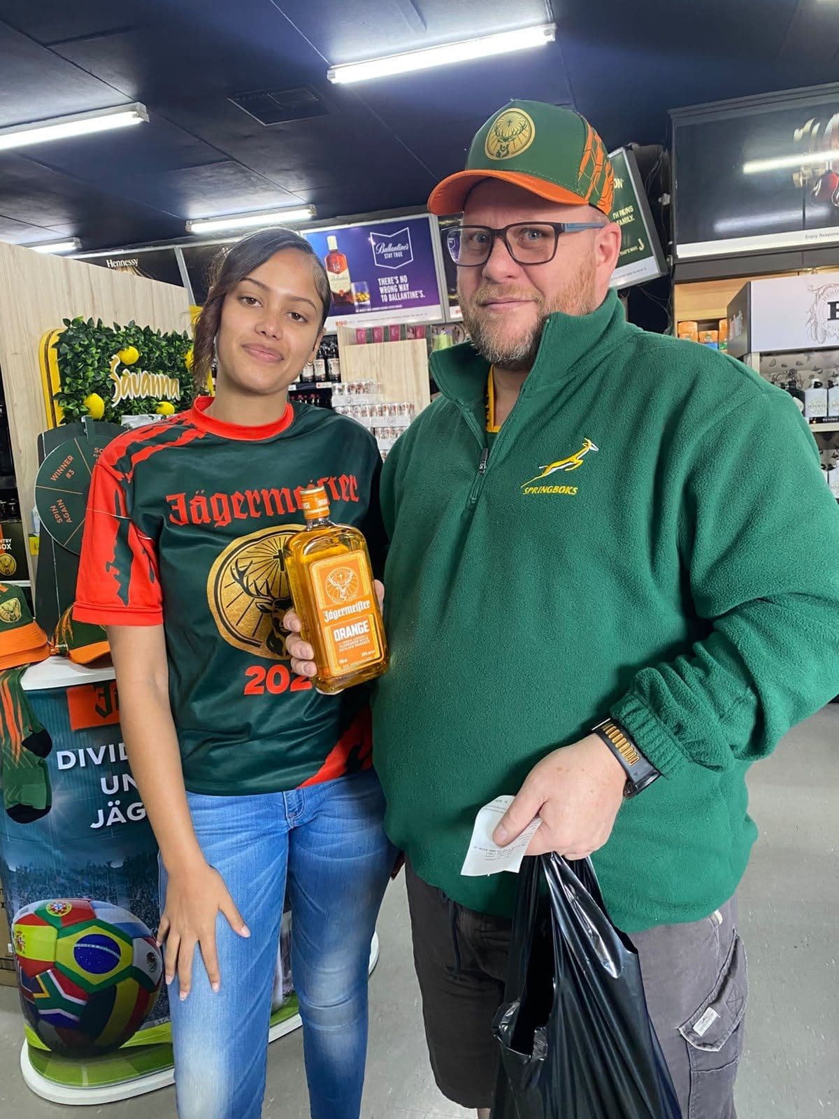 A promoter with a bottle beside an older shopper in a Springbok fleece