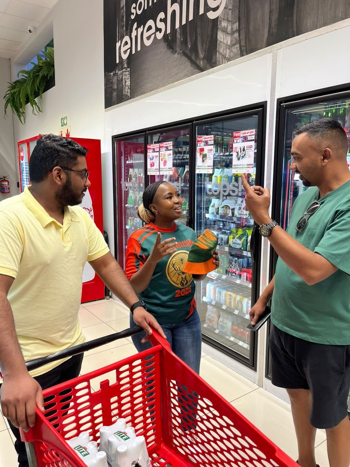 A promoter in conversation with two shoppers over a red trolley at the fridges