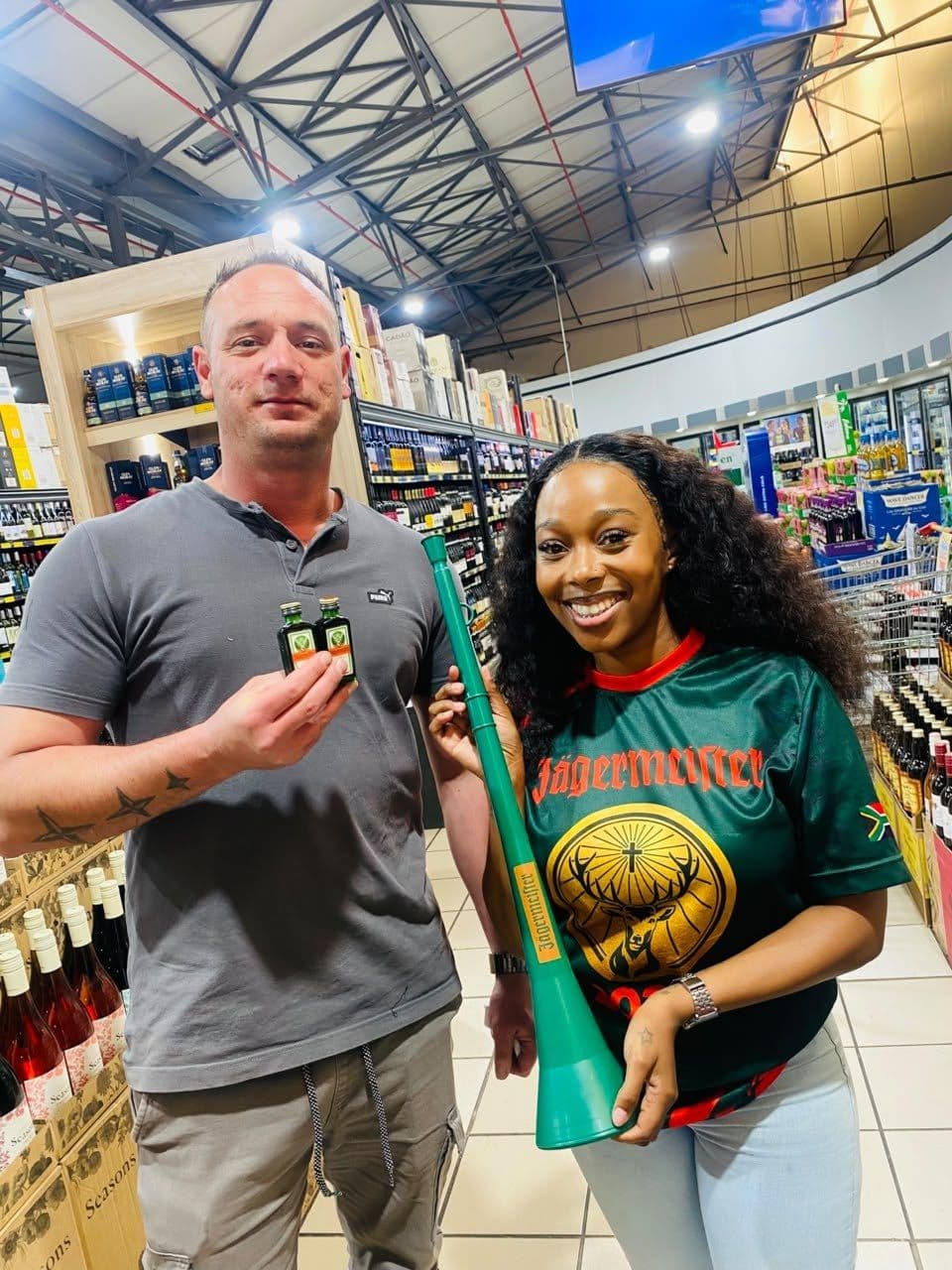 A promoter holding the green campaign flag beside a shopper, shelves behind