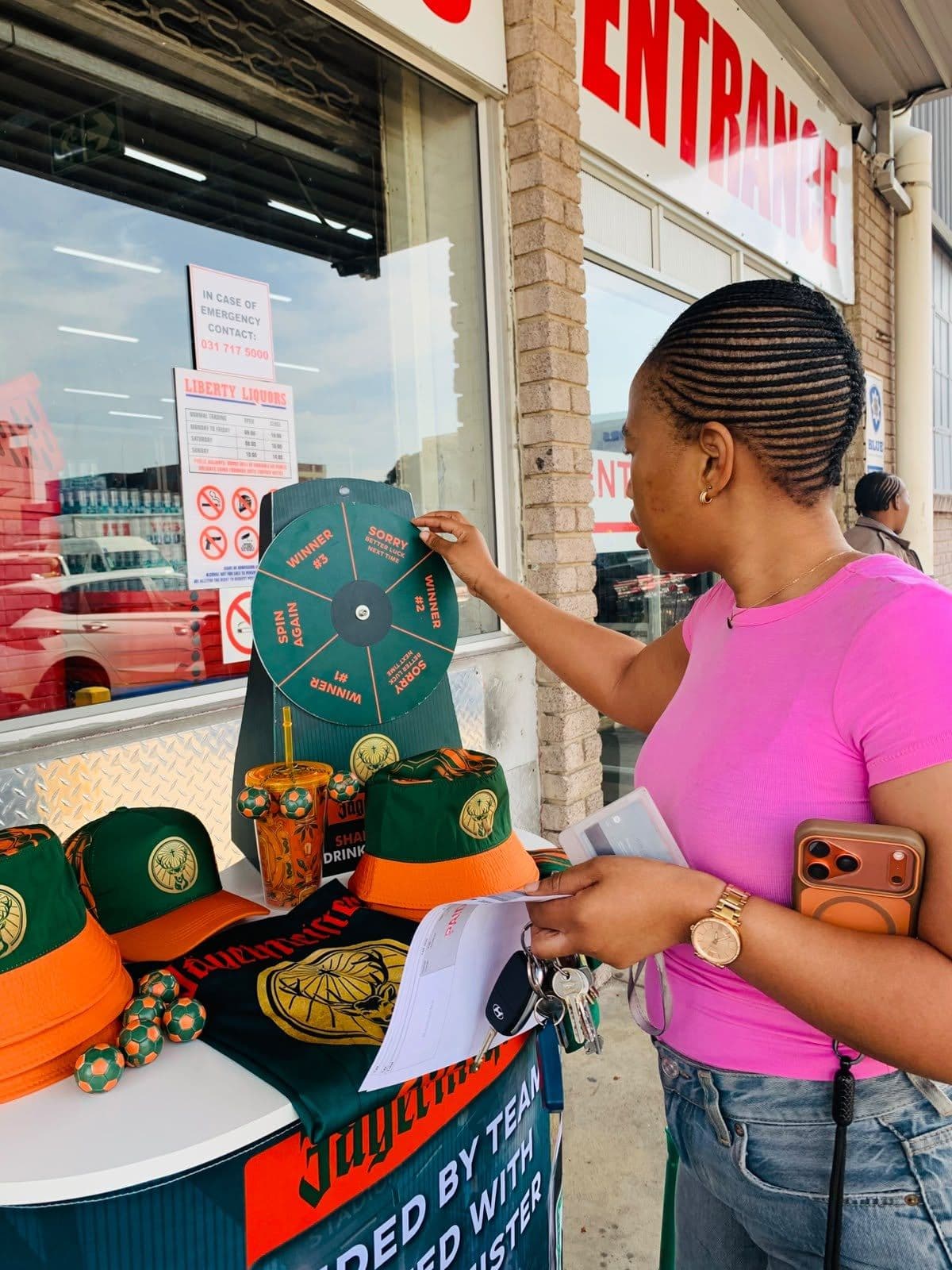 Two women at the merch table, one reading the campaign card, caps and jerseys laid out