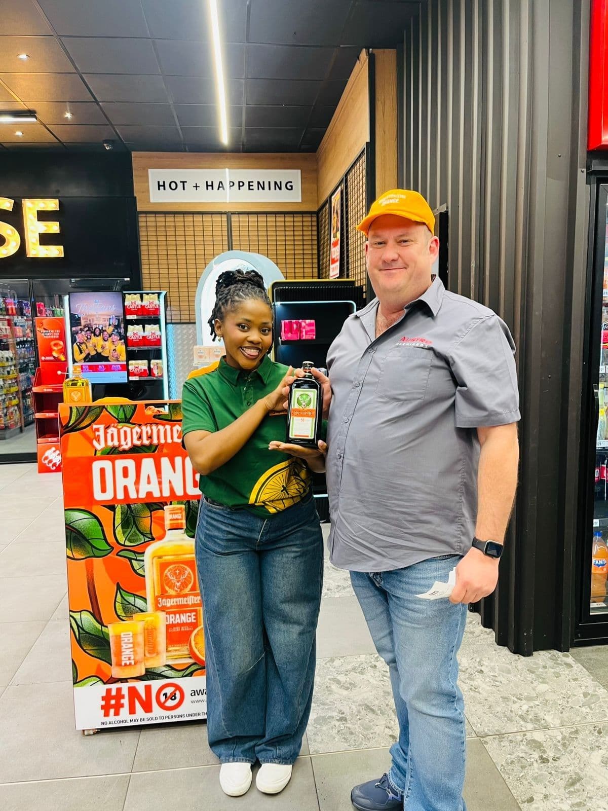 A promoter and a shopper in an orange cap at the Jägermeister Orange roll-up banner