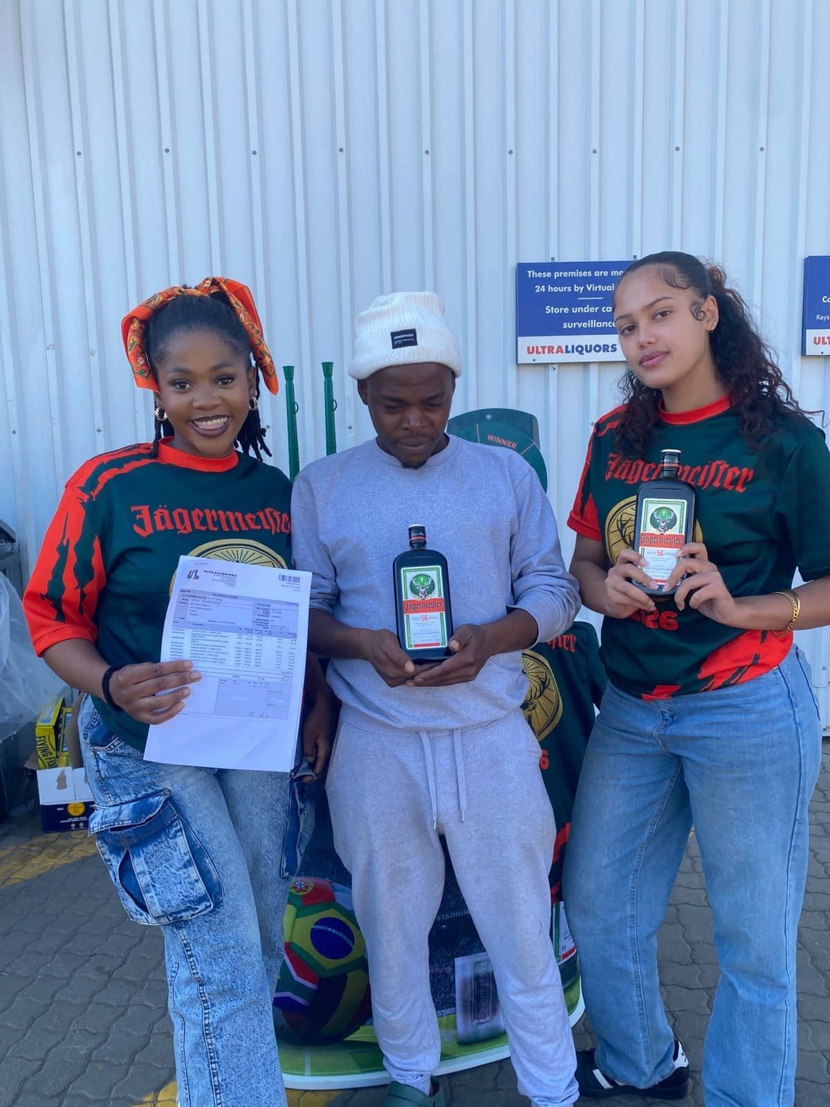 Two promoters in campaign shirts and a store worker with the delivery paperwork and a bottle at the receiving door
