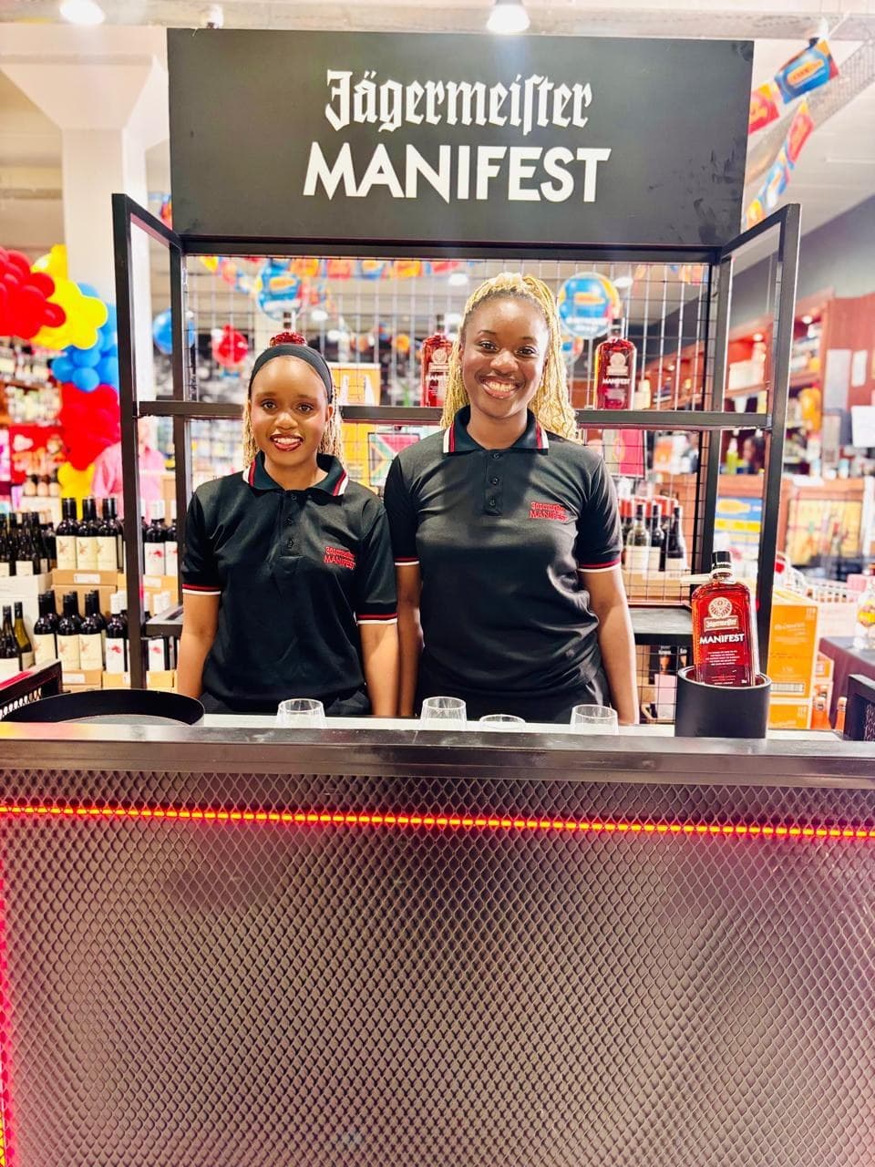 Two promoters in black Manifest kit behind the Jägermeister bar counter