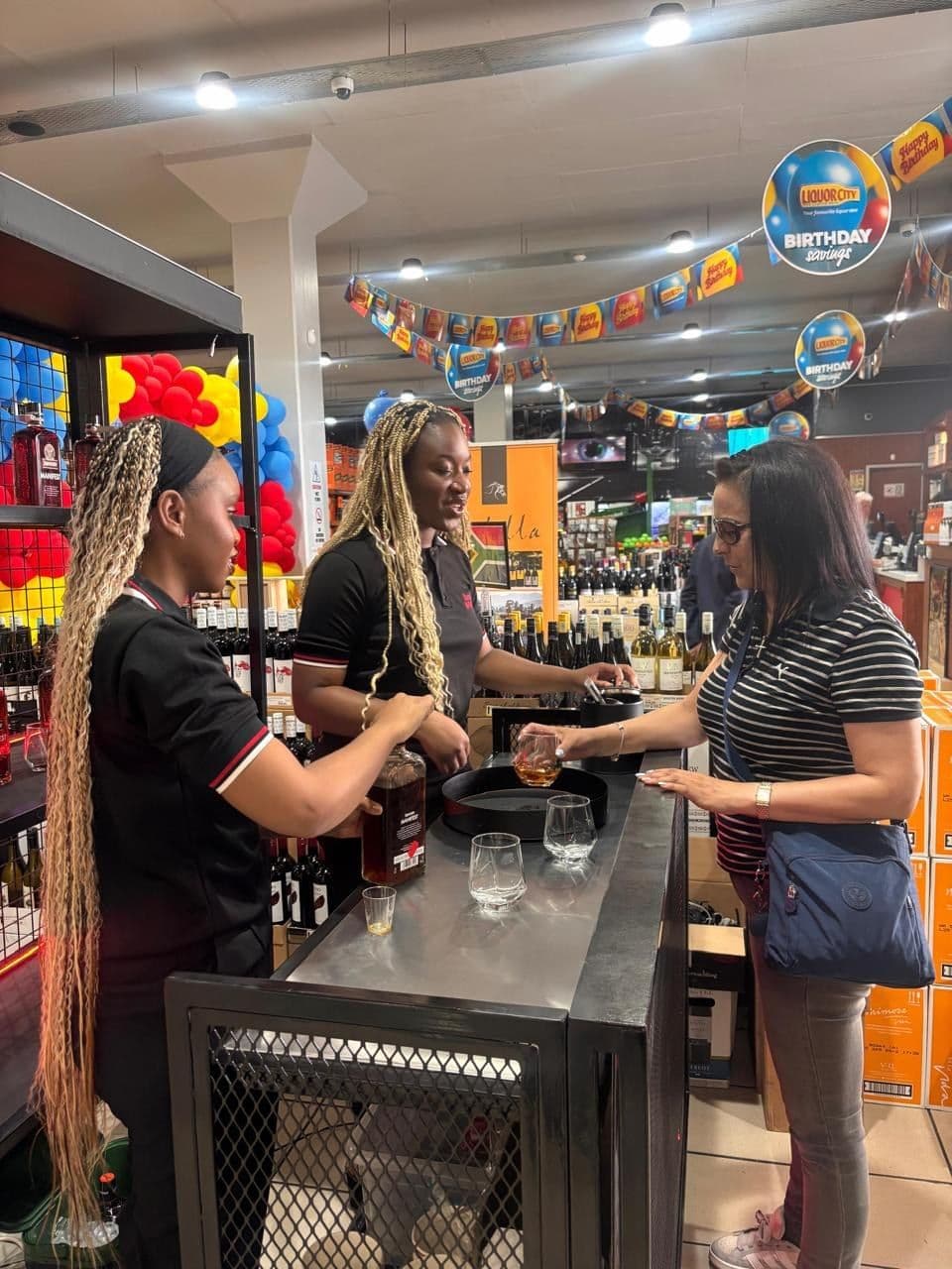 A promoter pouring a taste for a shopper across the bar counter, with more shoppers waiting alongside