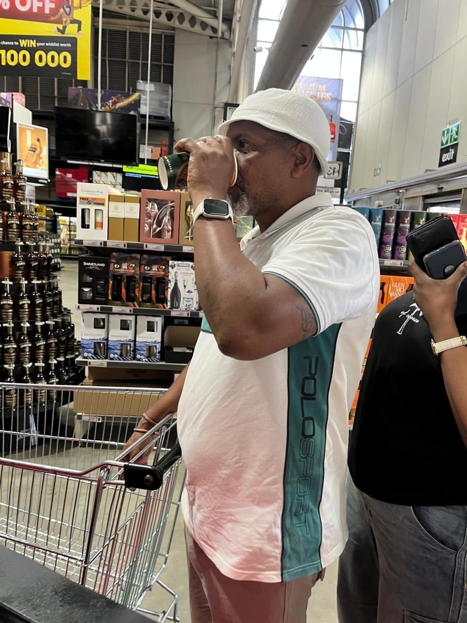 A shopper in a white bucket hat taking his first taste at the bar, the store aisle busy behind him