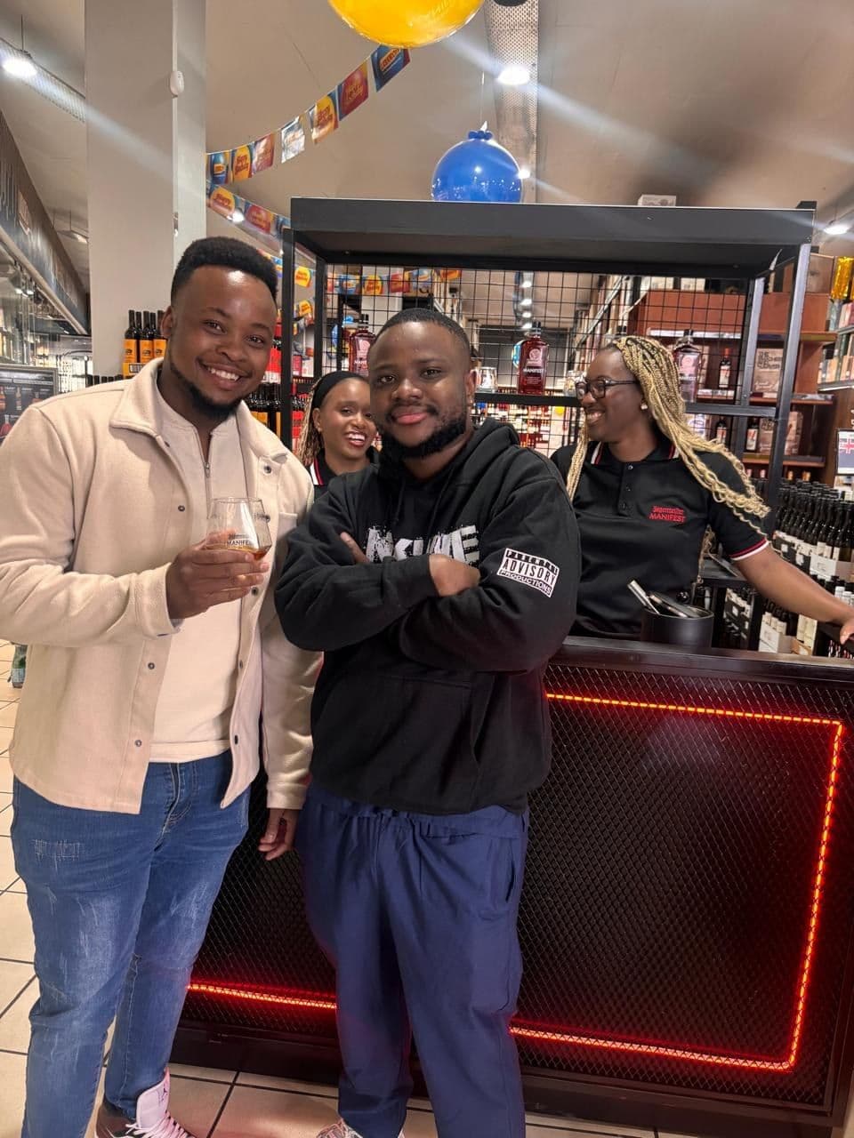 Two shoppers posing arm in arm at the bar rail with their serves, both grinning at the camera