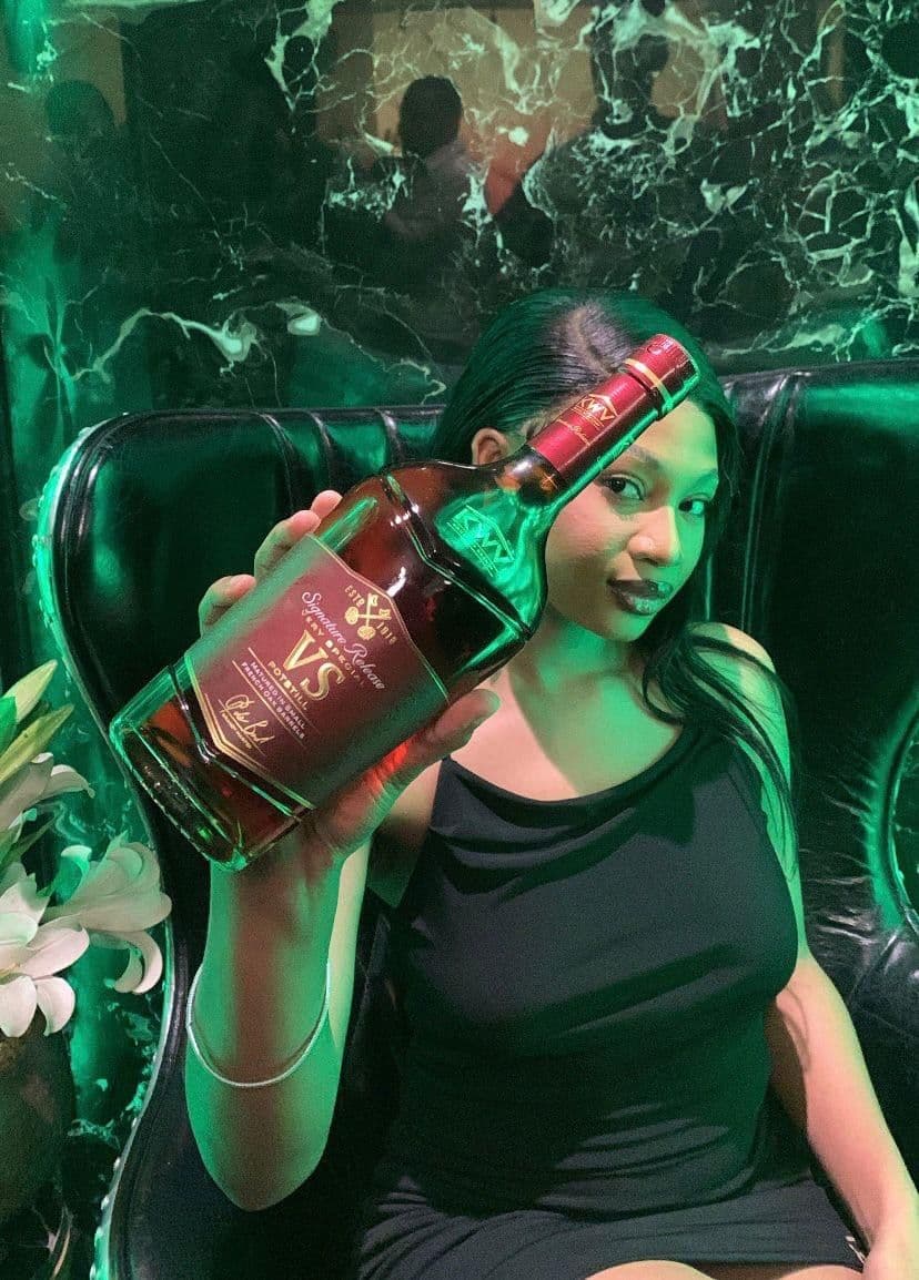 A model holding the bottle out toward the camera in the green-lit set