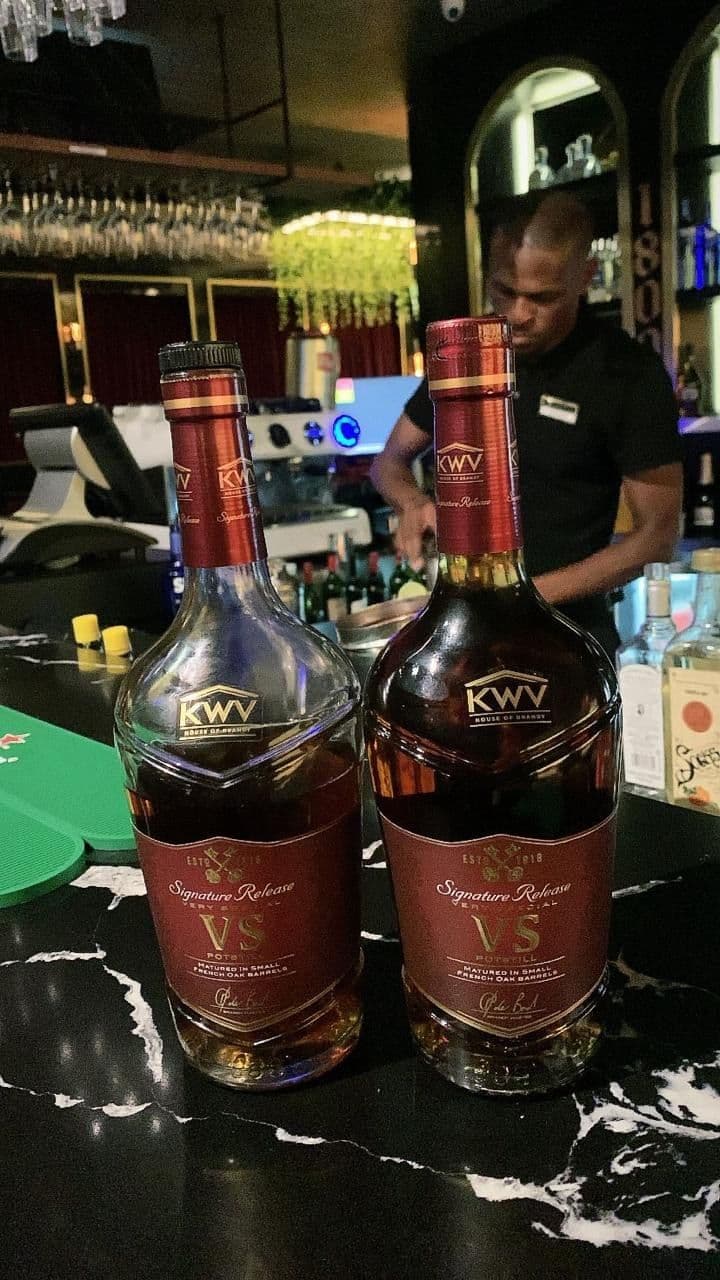 Two bottles of KWV VS Signature Release on the bar, the barman working behind them under green light