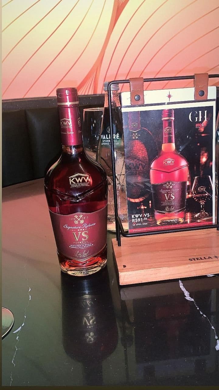A bottle of KWV VS beside the venue's menu card in its holder, the card carrying the bottle, the price and the date 24 April 2026